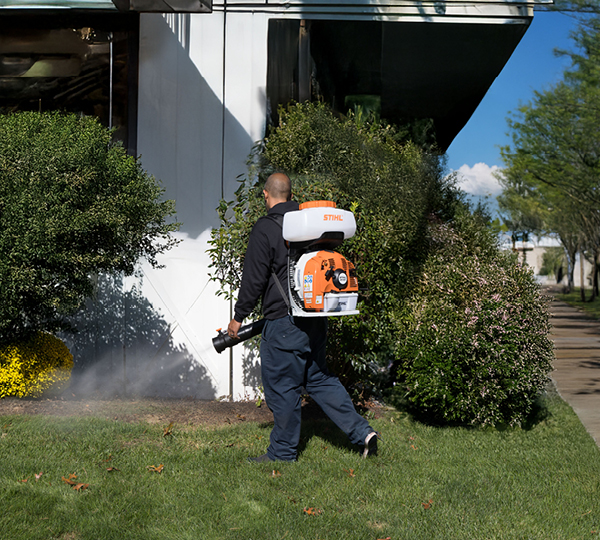 Professional pest control technician on property applying a spray organic mosquito and tick prevention treatment for home, yard, and garden.